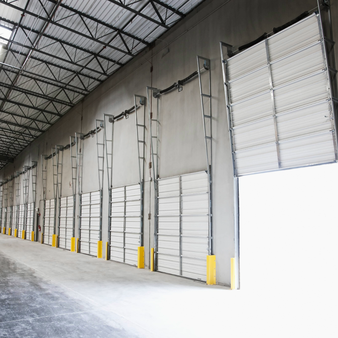 Interior of a commercial warehouse with multiple overhead garage doors, including one open door.