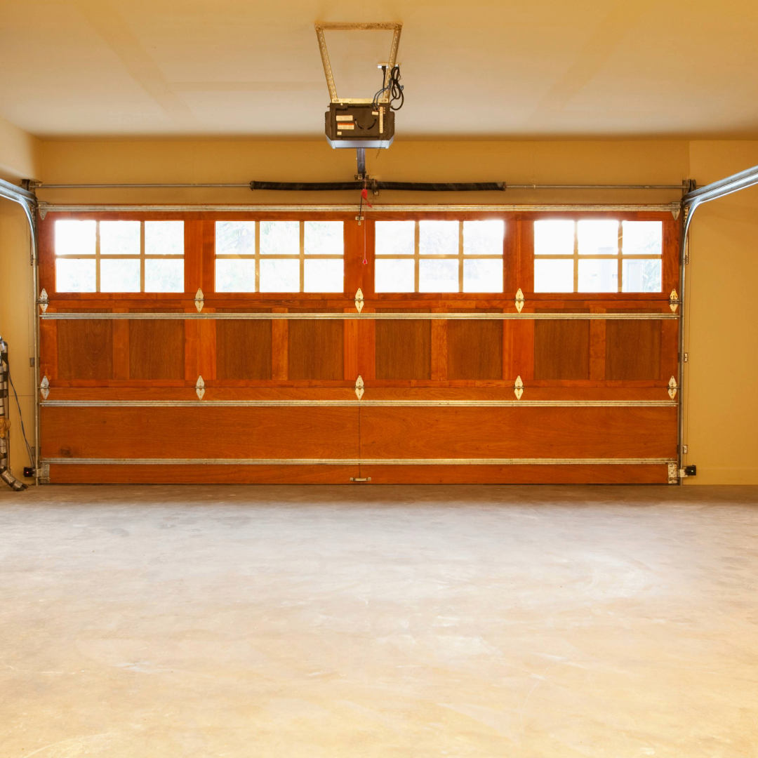 Interior view of a residential garage with a closed wooden garage door and ceiling‑mounted opener.